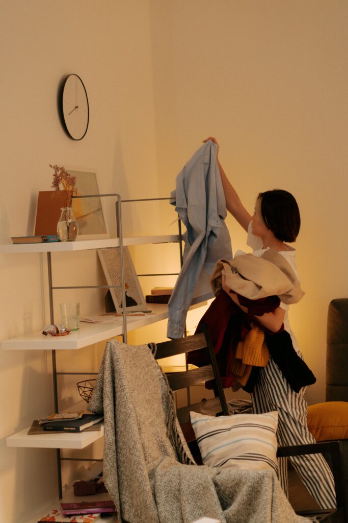 pexels photo 7703297 7703297 A woman tidying up clothes in a warm, cozy bedroom setting indoors.